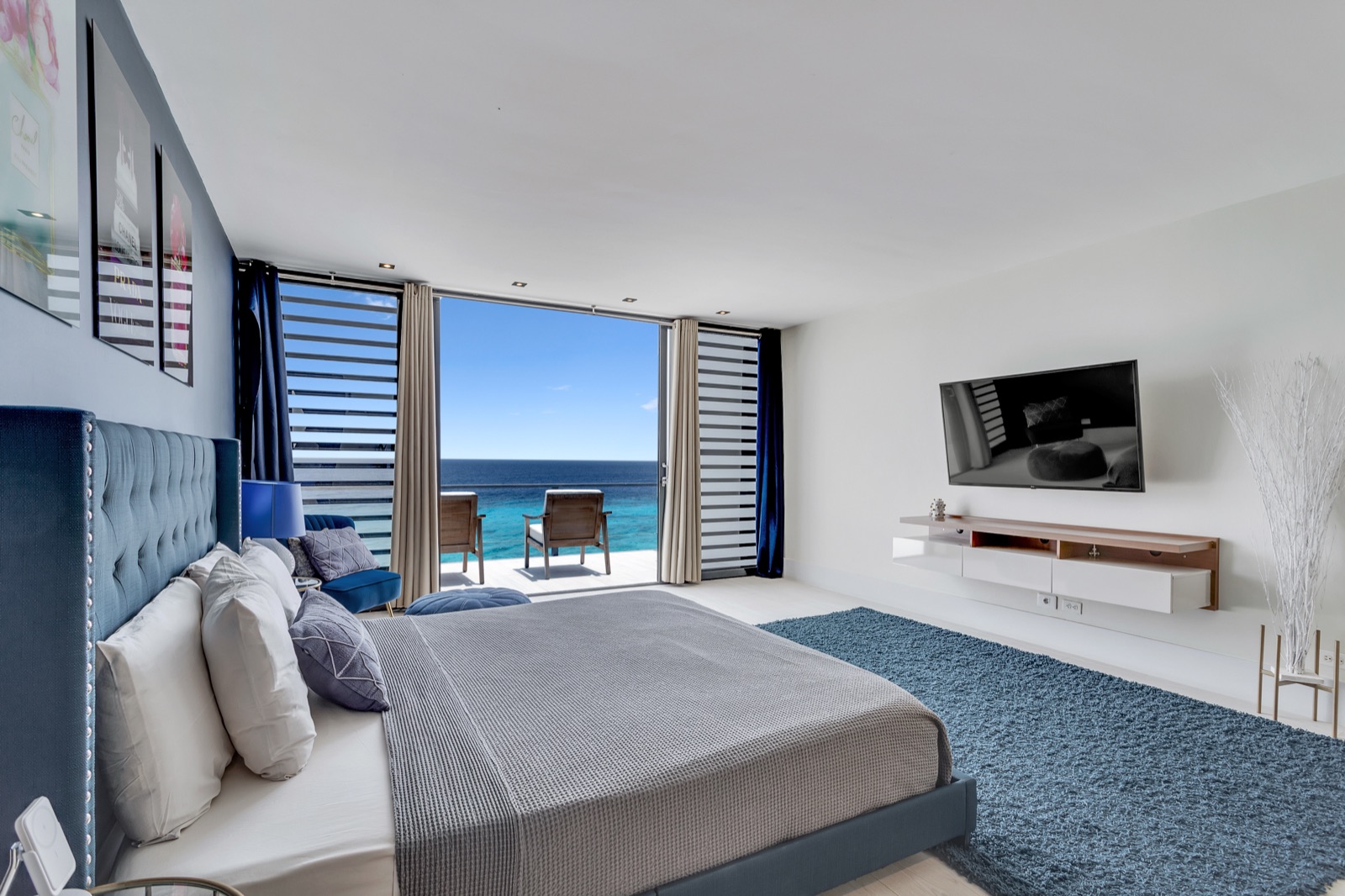 Luxury Bonaire villa master suite with blue tufted king bed, opening onto a private balcony with stunning panoramic ocean views.